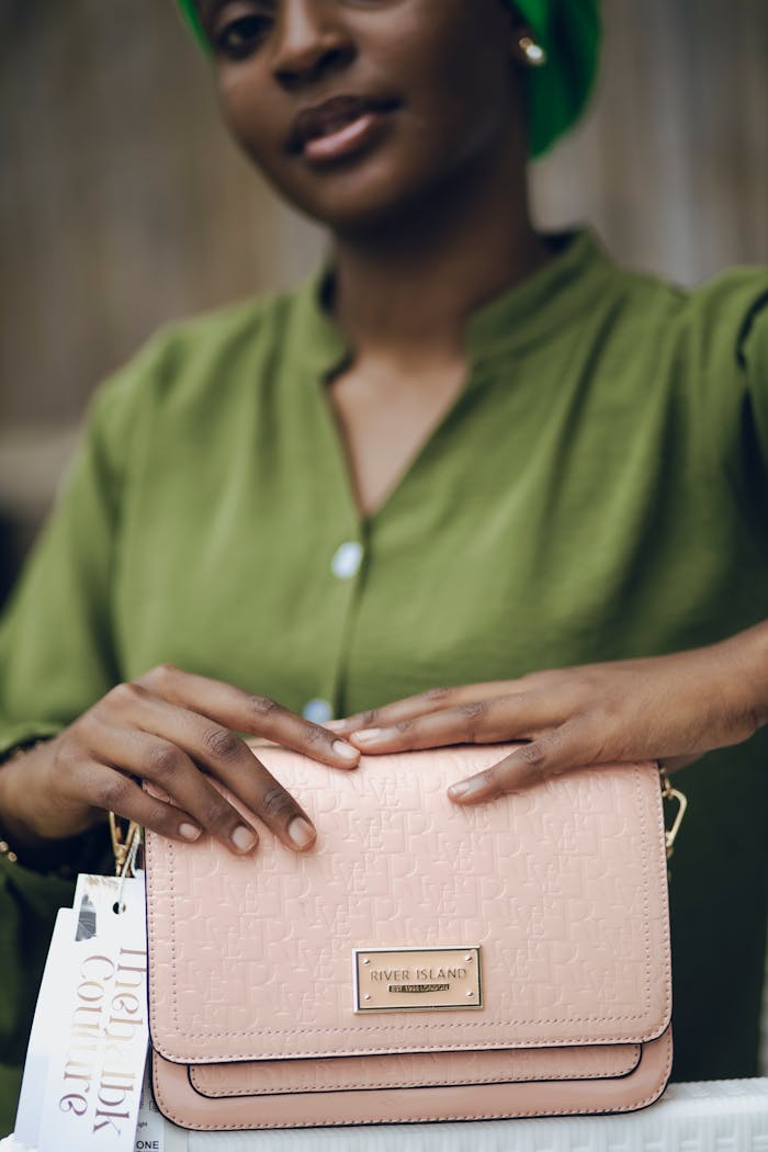 Close-up of a woman showcasing a sophisticated designer handbag in soft lighting.