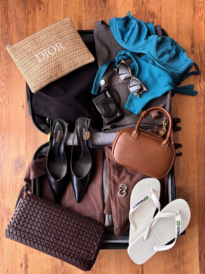 Flat lay of fashion and travel essentials in an open suitcase on wooden floor, ready for vacation.